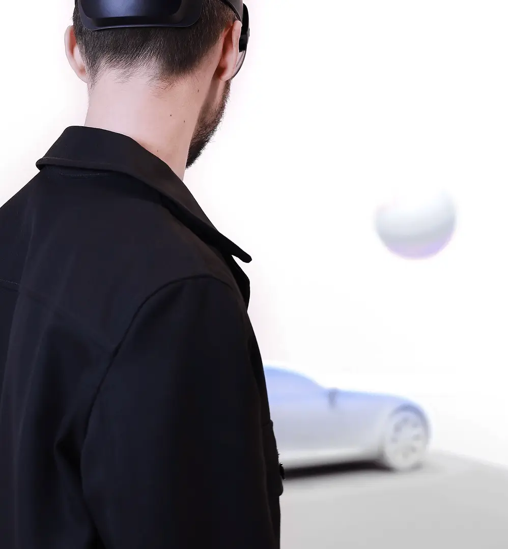 A man in the foreground with a virtual orb floating above a model car in the background.
